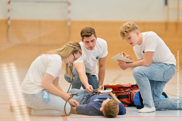 Mitglieder eines Schulsanitätsdienstes bei der Ersten Hilfe in einer Sporthalle.
