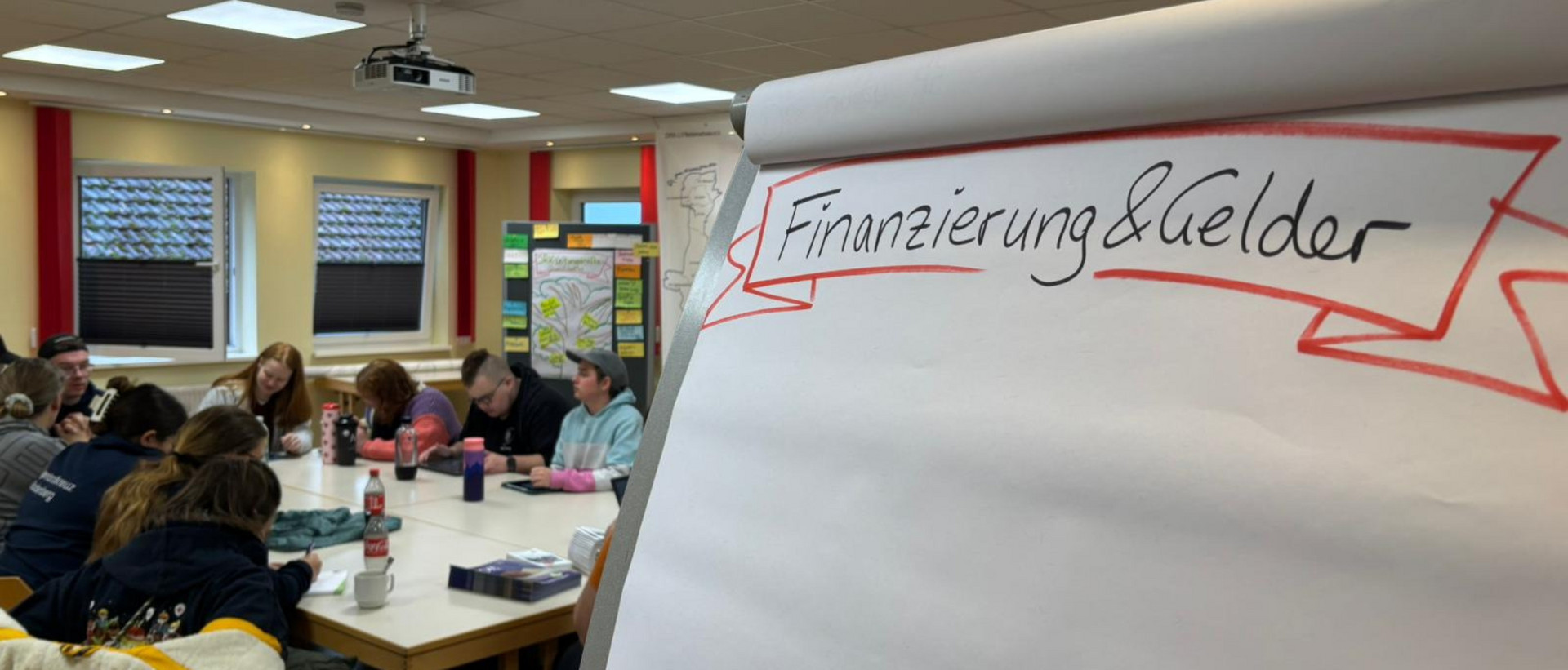 jrk-nds_fördermittel_titelbild.jpg Eine Flipchart mit der Überschrift Finanzierung und Gelder steht in einem Seminarraum mit JRK-Mitgliedern.