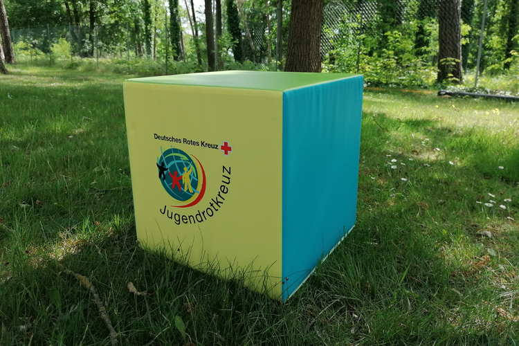 Ein Sitzwürfel mit JRK-Logo, bei dem jede Seite in einer anderen JRK-Farbe gestaltet ist.