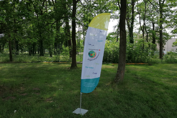 Eine Beachflag mit dem Wort "Hallo" in verschiedenen Sprachen und dem JRK Logo.